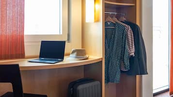 Une chambre d’hôtel équipée d’un bureau, d’un ordinateur portable, d’une valise et d’un portant à vêtements sur lequel sont disposés différents vêtements.