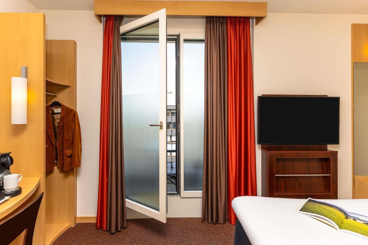 Ein Hotelzimmer mit einem Bett, einem Fernseher, einem Schreibtisch mit Kaffeemaschine und einem Kleiderschrank.