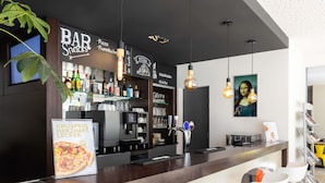 A bar area with a counter, bar stools, shelves with bottles, and a menu stand. - ibis Basel Bahnhof (Basel)