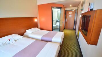 A hotel room with two beds, a television, and a bathroom visible through an open door.