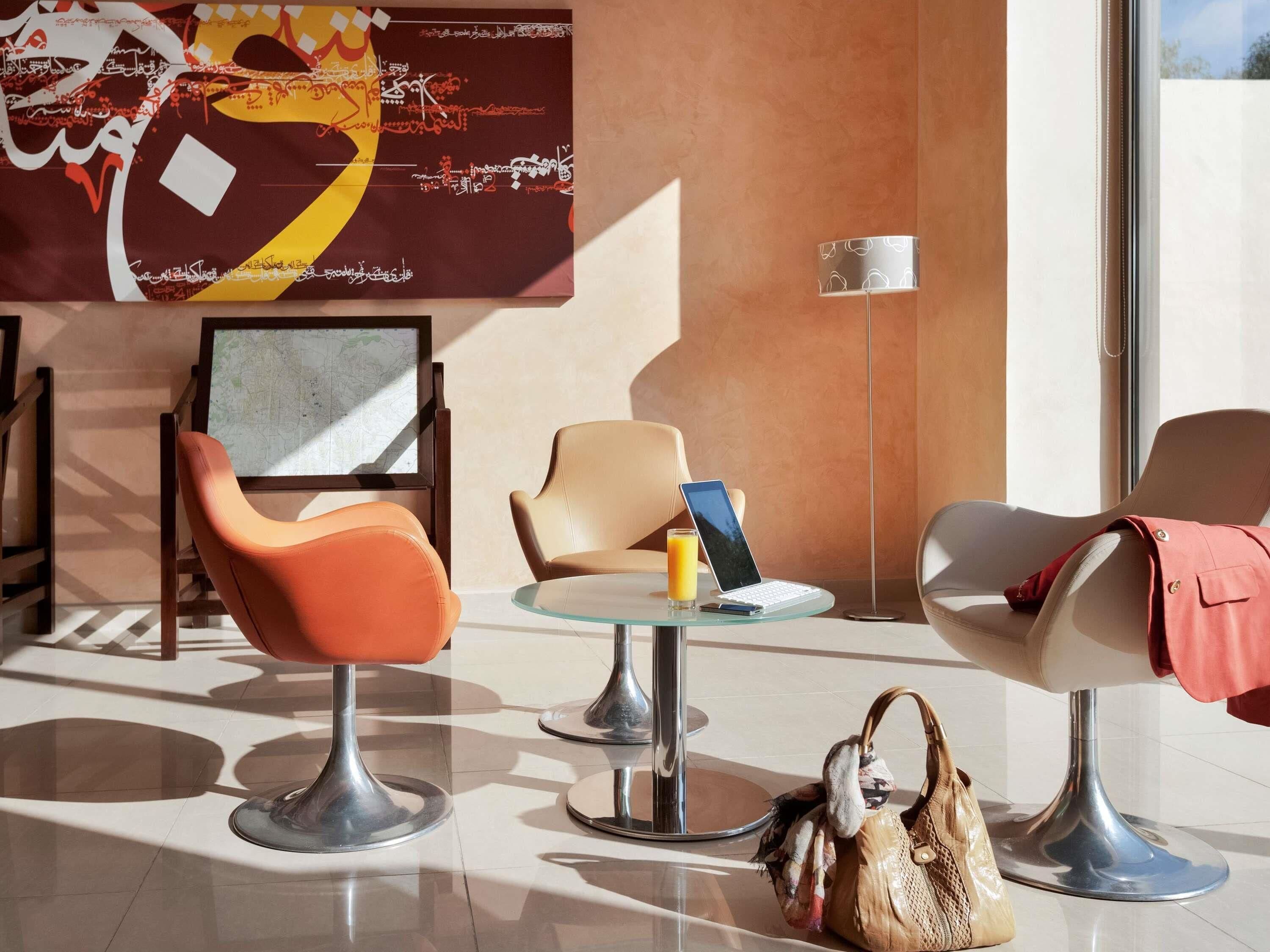 A modern lobby with a map on the wall, a glass table with a laptop, a glass of orange juice, and a handbag on the floor.