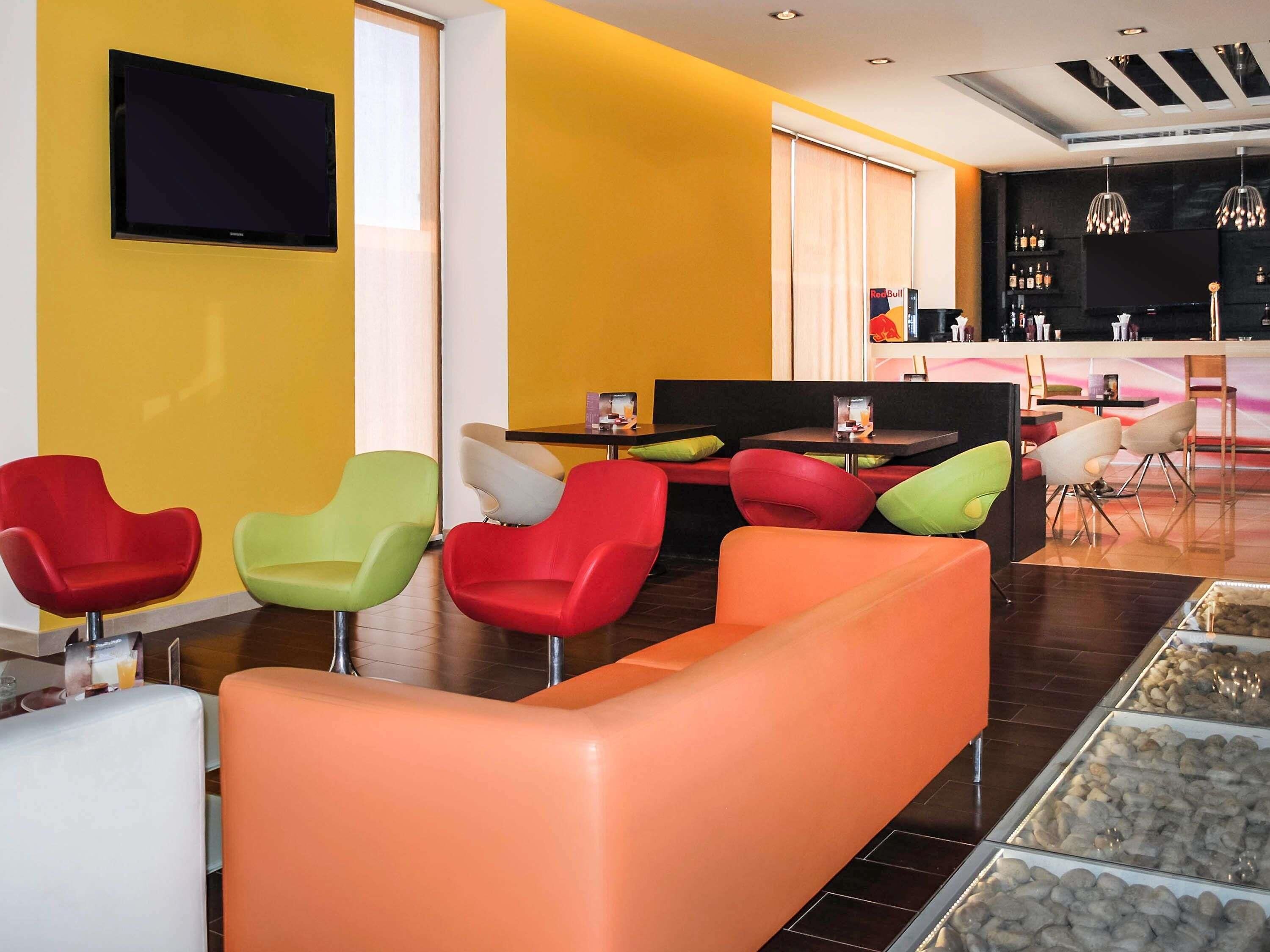 Un hall d'hôtel moderne avec des sièges aux couleurs vives, un téléviseur à écran plat et un espace bar.