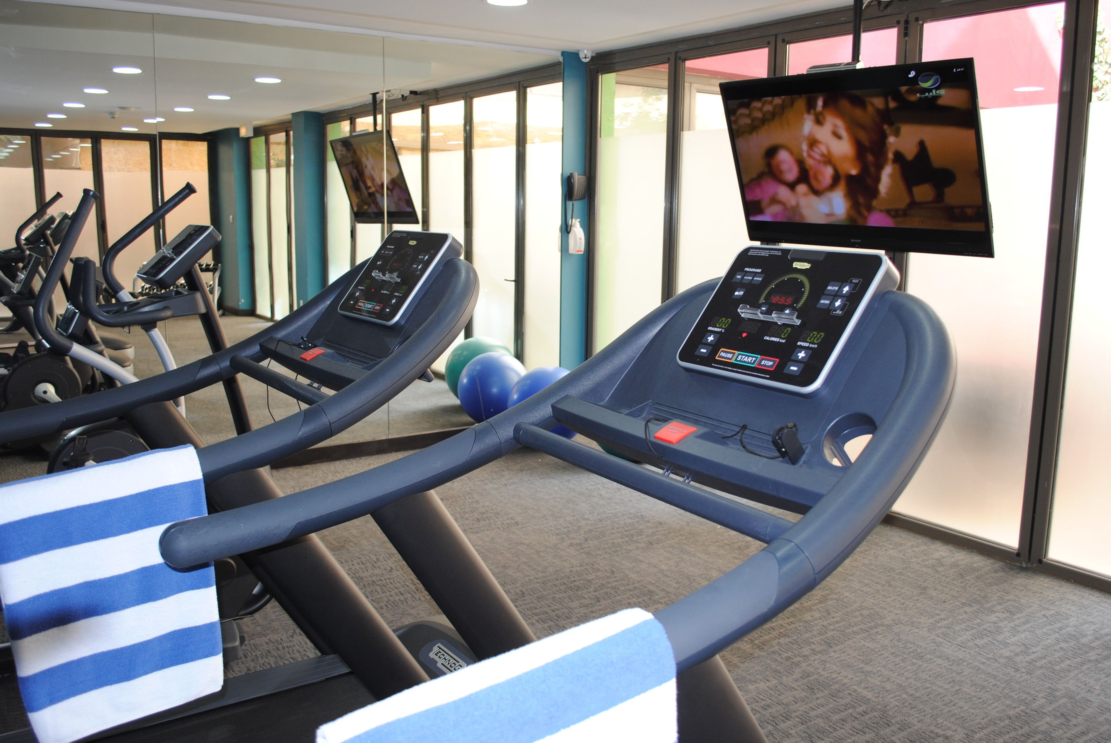 Un gimnasio con cintas de correr, una bicicleta estática y una pantalla de televisión mostrando un programa.