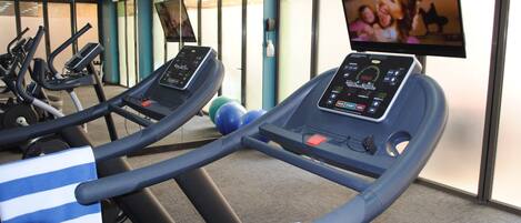 Un gimnasio con cintas de correr, una bicicleta estática y una pantalla de televisión mostrando un programa.