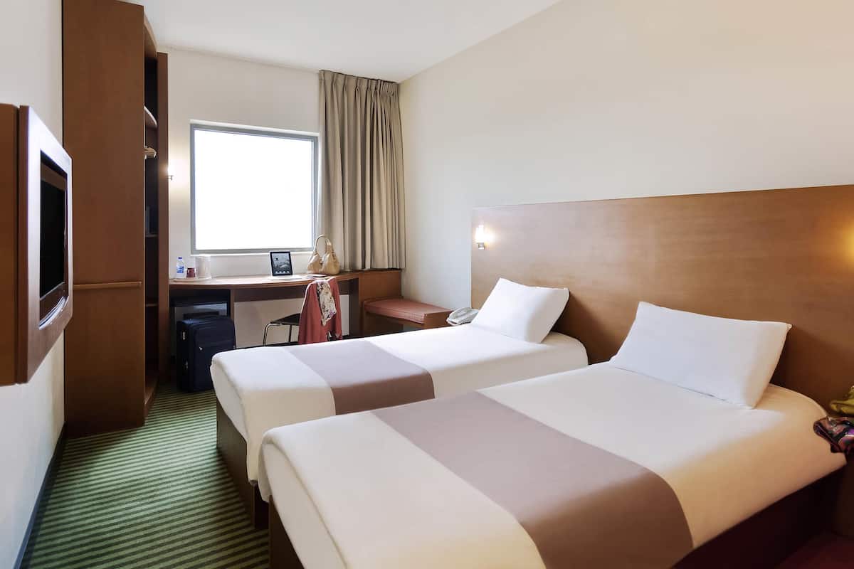 Habitación de hotel con dos camas, un escritorio, una silla, un armario y una ventana con cortinas.