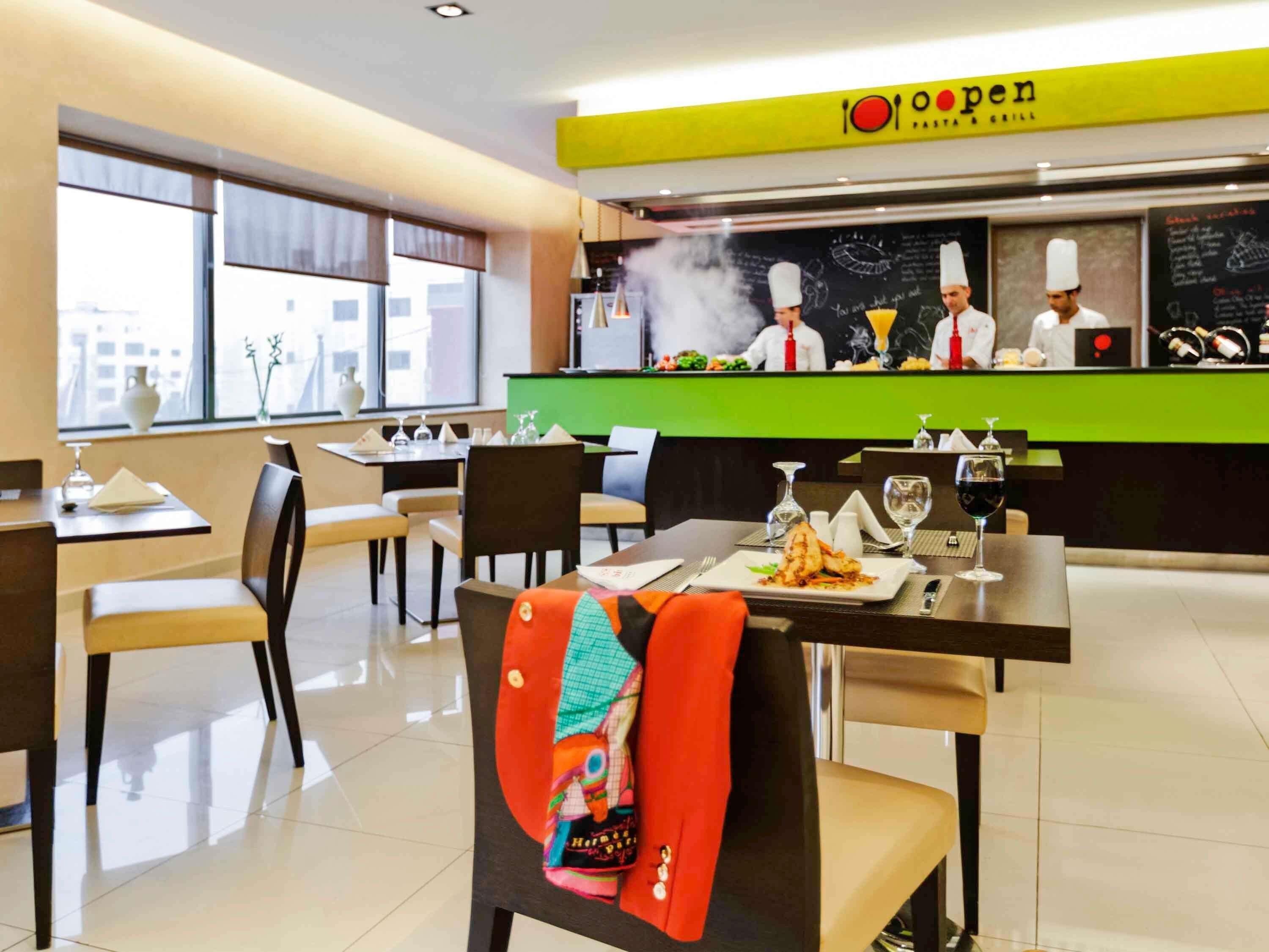 A restaurant interior with tables, chairs, a counter with chefs, and a menu board.