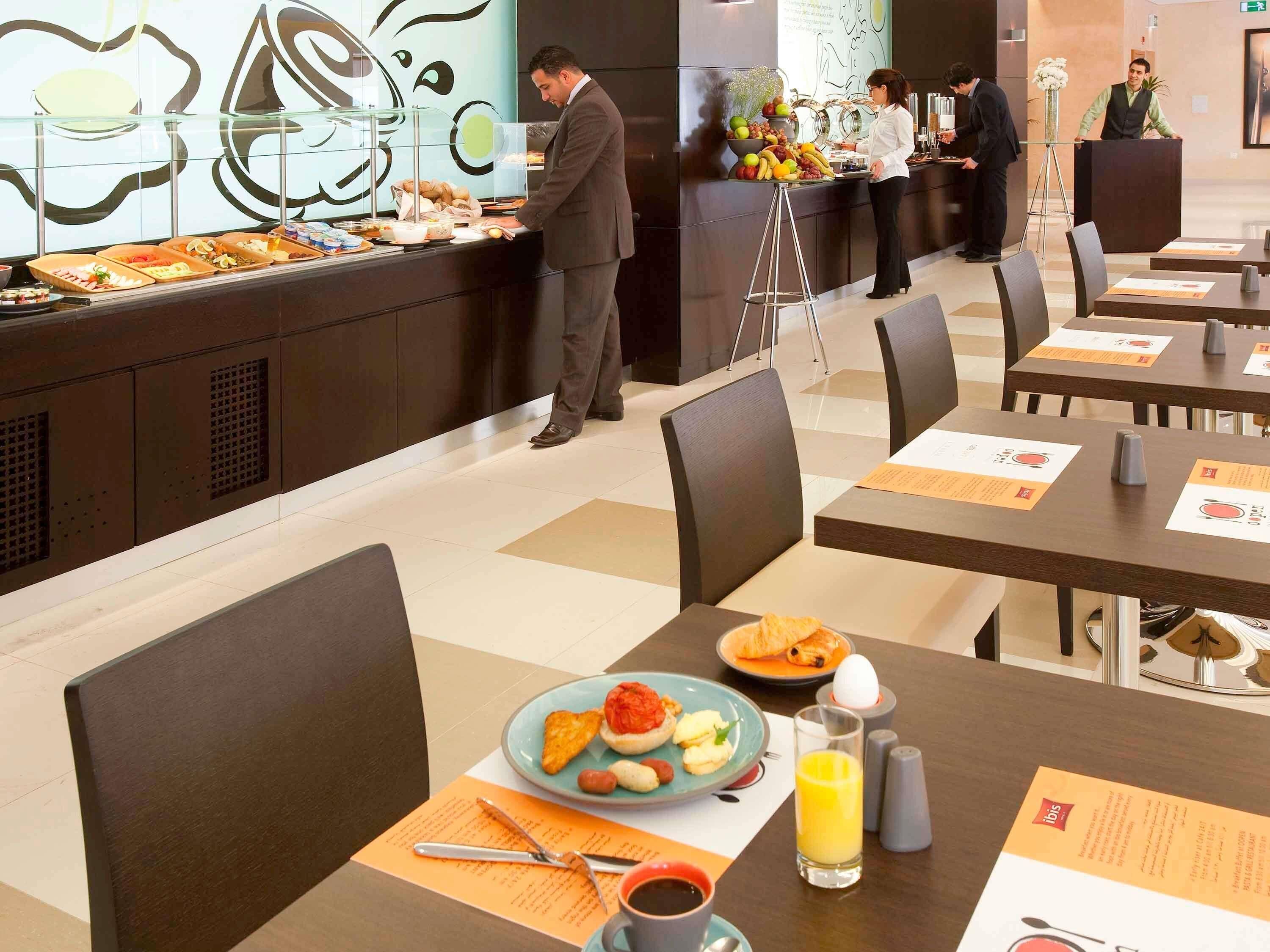 A hotel breakfast area with buffet service, dining tables, and chairs.
