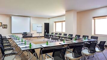 Un salón de conferencias con varias mesas, sillas, una pizarra y una pantalla de proyector.