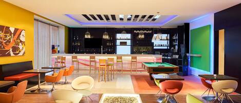 Zona de bar moderna con mesa de billar, asientos y barra.