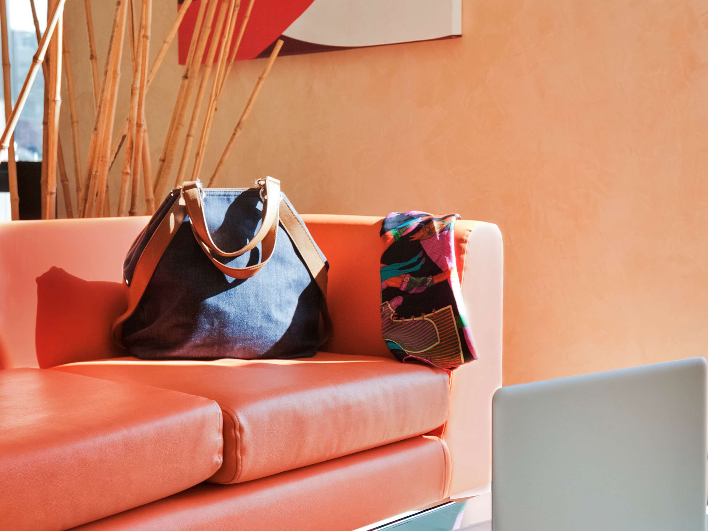 Una sala moderna con un sofá de cuero, una computadora portátil y dos bolsos.