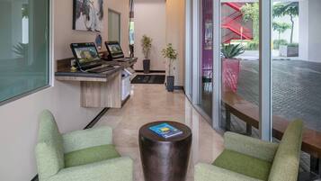 Un vestíbulo moderno con un mostrador de recepción, dos sillones verdes, una mesa de centro y una escalera con barandillas rojas.