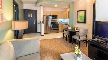 A compact living space with a sofa, a dining table with chairs, a TV, a kitchen area with a refrigerator and microwave, and a lamp.