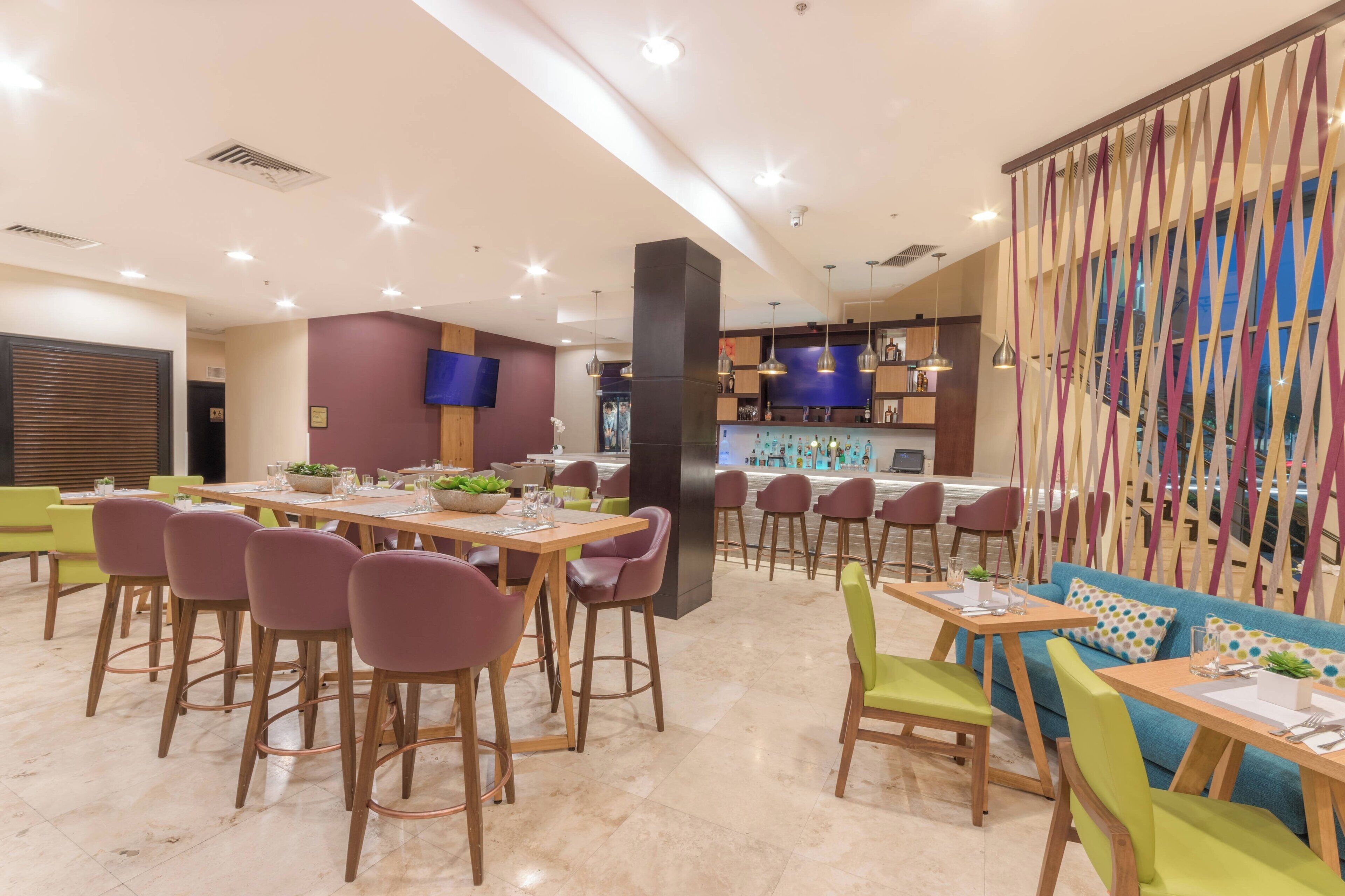 Een modern restaurant met verschillende eetgedeeltes, waaronder een bar en een zithoek met een kleurrijke scheiding.