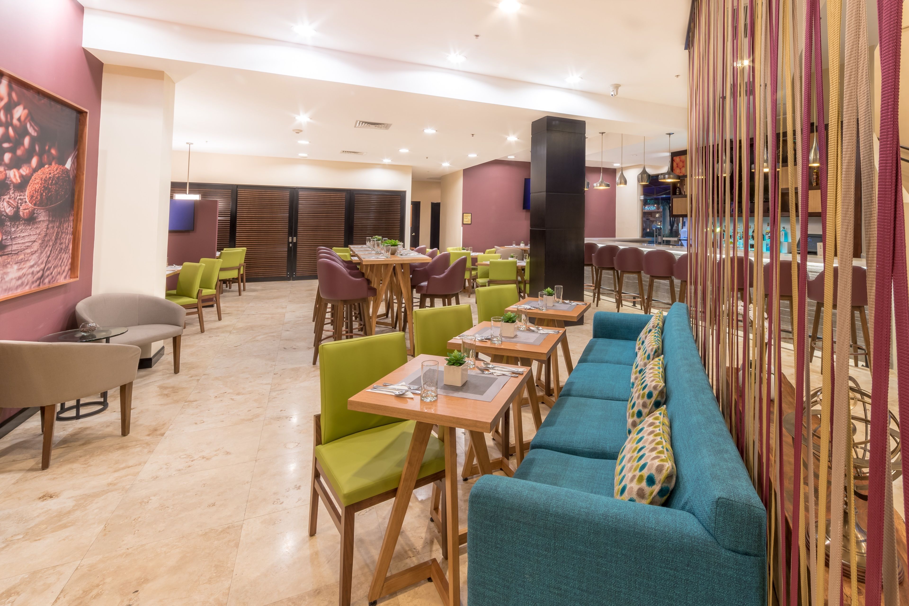 A modern dining area with green and blue seating, wooden tables, and a large black pillar.