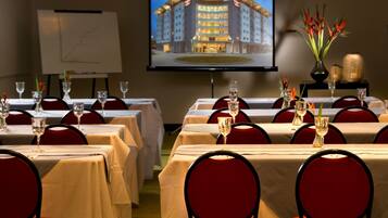 A conference room with tables set for a meeting, a projection screen displaying a building, and a whiteboard with a graph.