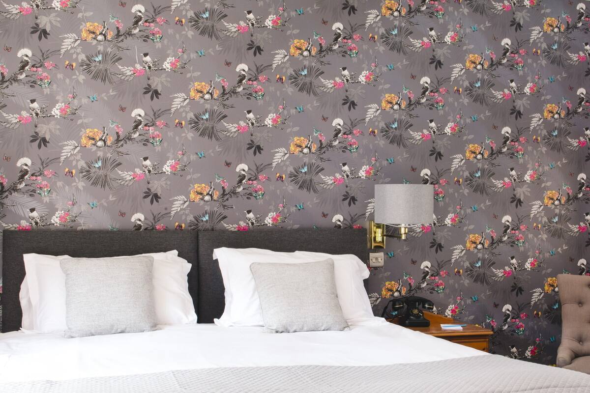 A hotel room with a large bed, a nightstand, a lamp, a chair, and a framed picture on the wall.