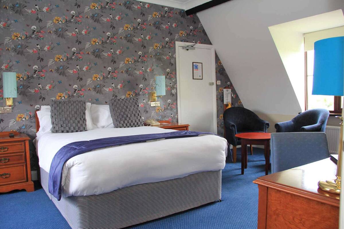 A bedroom with a bed, a desk, a chair, and a small table.