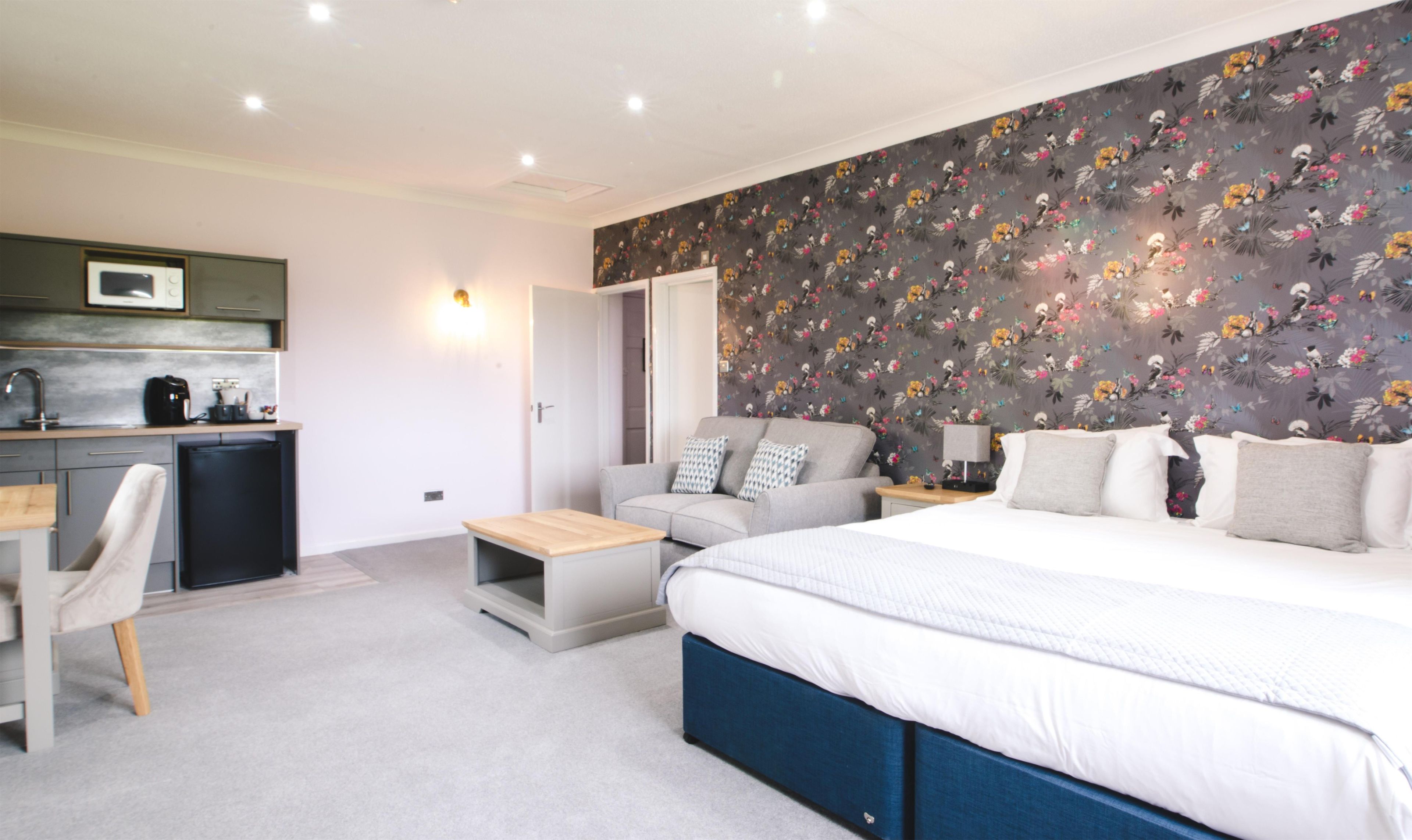 A bedroom with a large bed, a sofa, a desk, and a kitchenette.