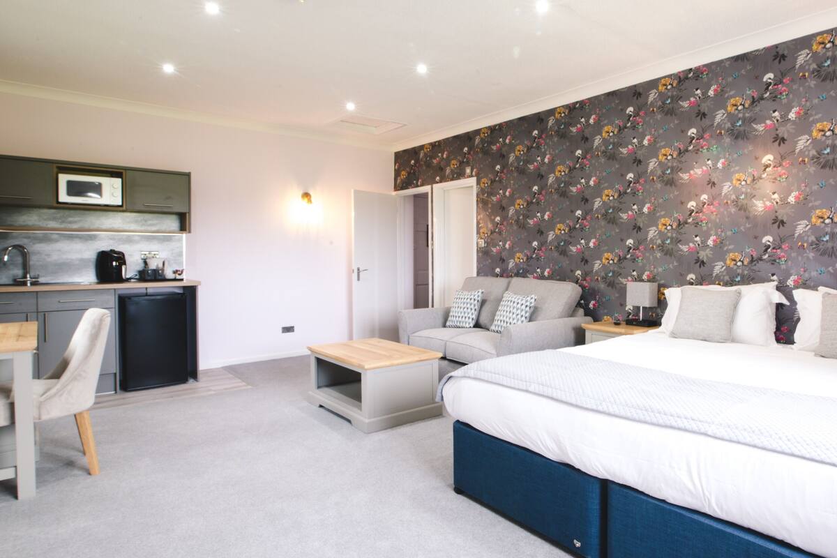 A modern bedroom with a large bed, a sofa, a desk, and a kitchenette.
