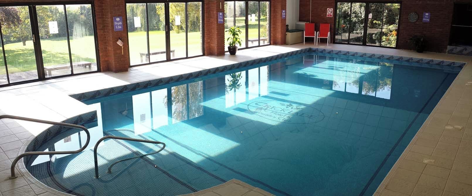 Una piscina interior amb parets de vidre transparent, un terra emblamat i una banca a l'exterior.