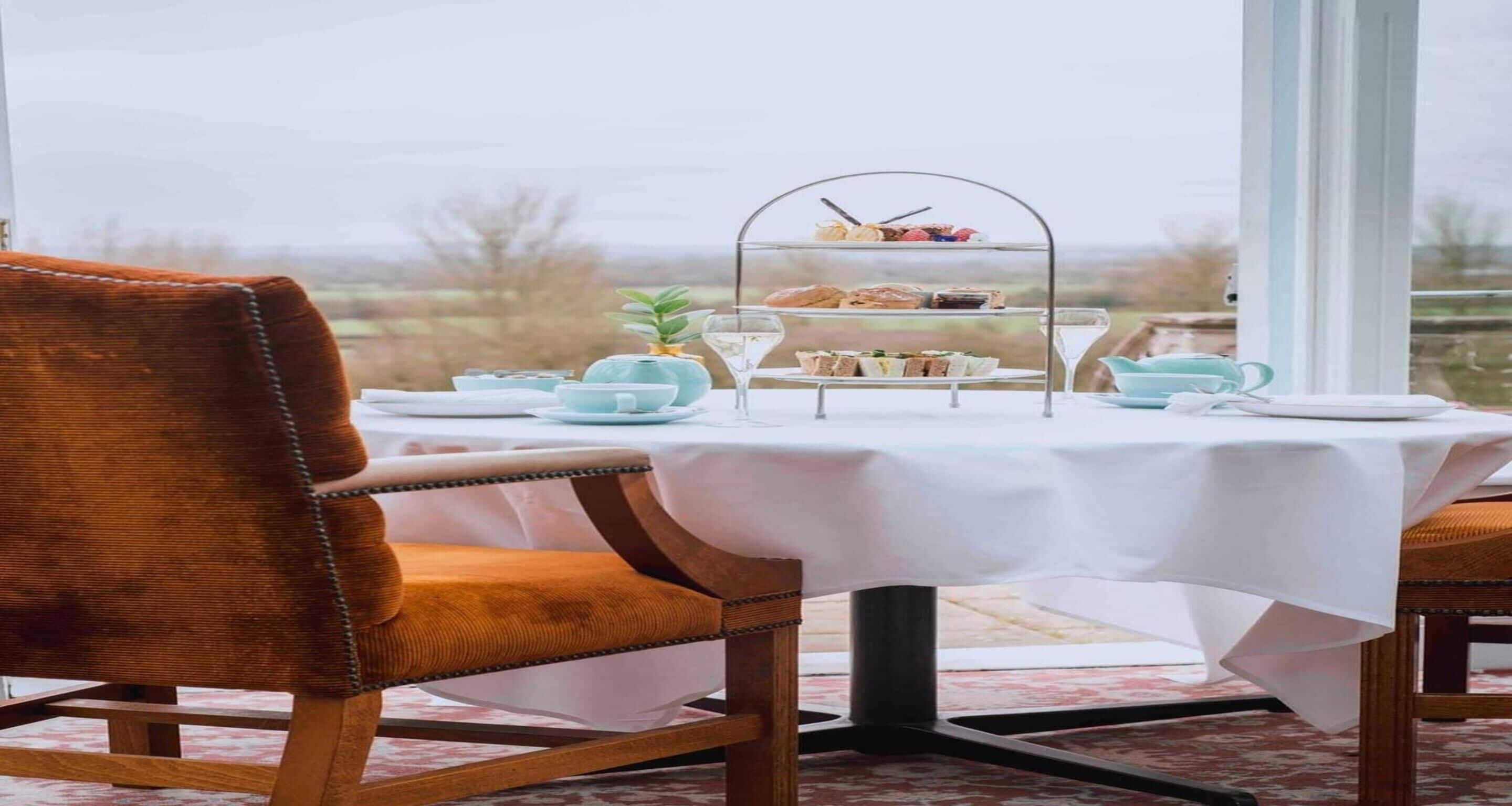 A dining table with a white tablecloth, a tiered dessert stand, and a view of the outdoors.
