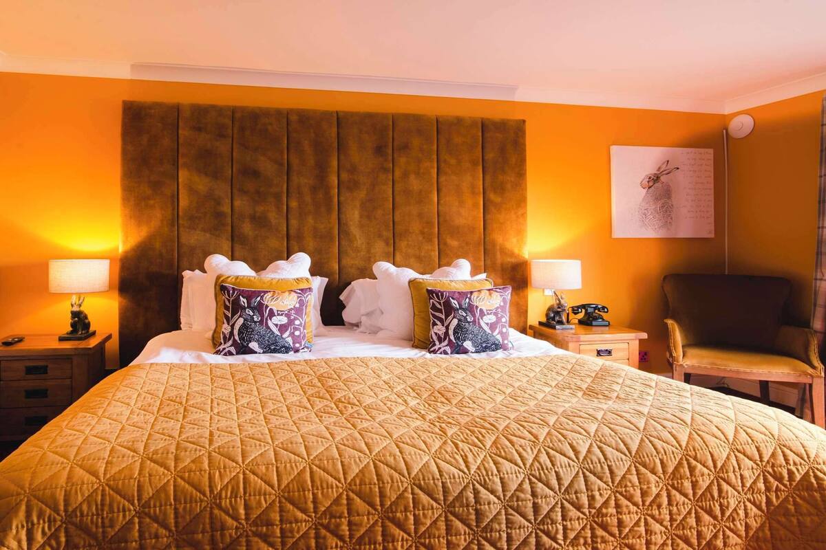 A hotel room with a large bed, two bedside tables, a chair, and a wall-mounted shelf.