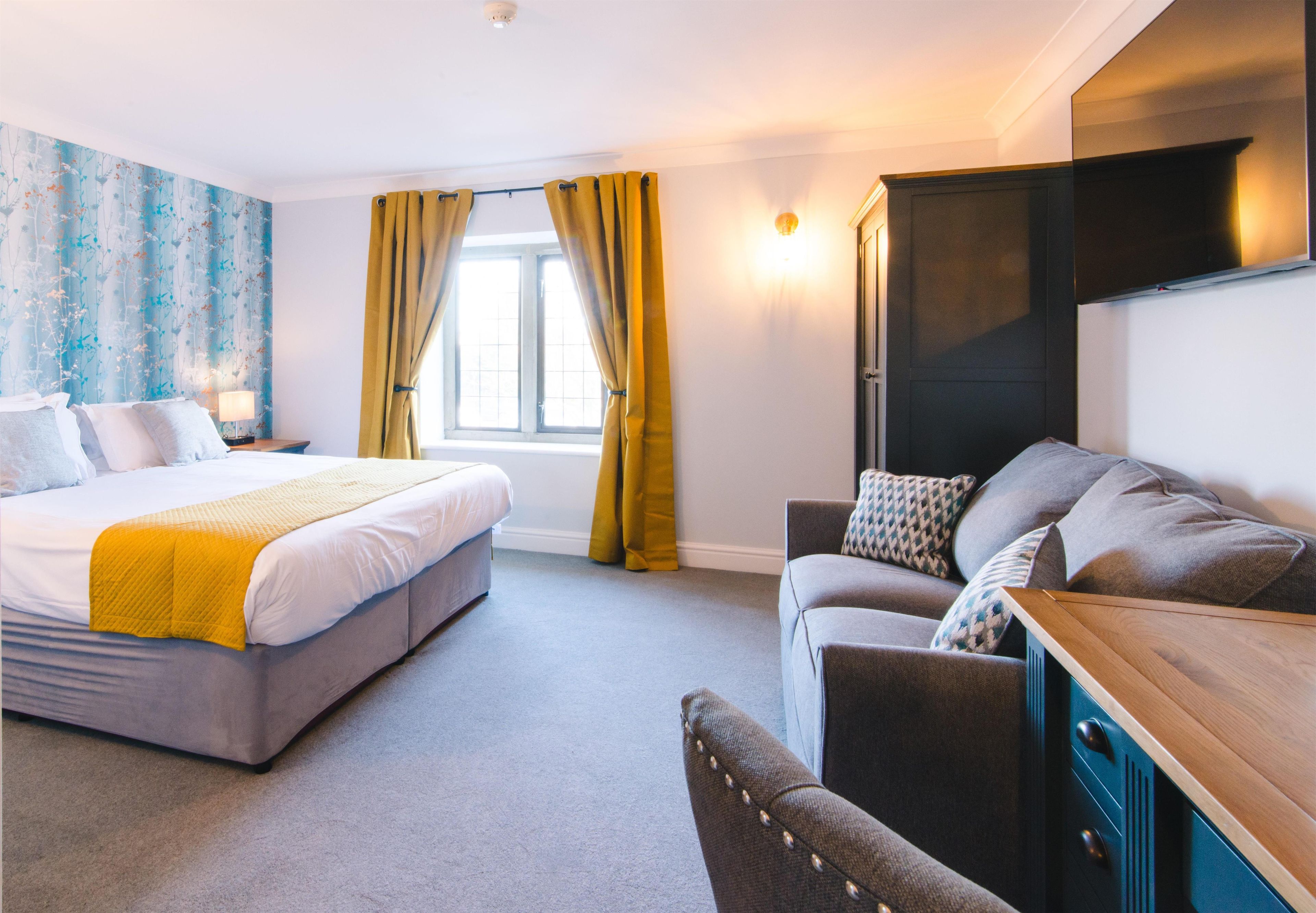Une chambre d’hôtel avec un lit, un canapé, un bureau et une fenêtre avec des rideaux.