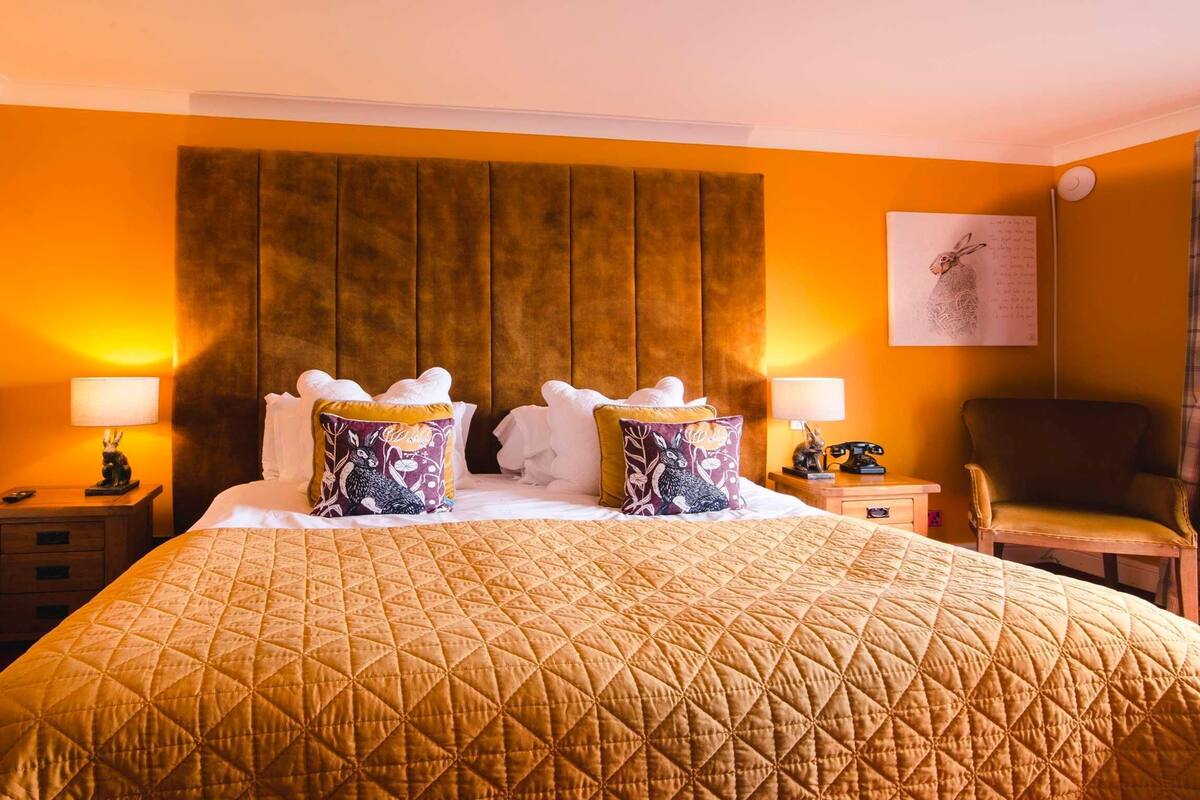 A hotel room with a large bed, two bedside tables, a chair, a wall-mounted lamp, and a radiator.