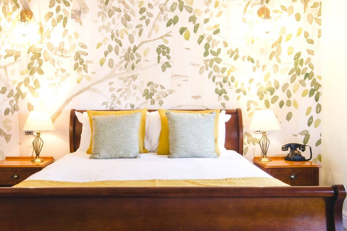A bedroom with a bed, two nightstands, a lamp on each nightstand, and a wall with a leaf pattern.