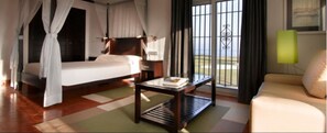 A hotel room with a bed, a small table, a sofa, and a view of the outdoors through large windows. - Parador de Málaga Golf  (Málaga)
