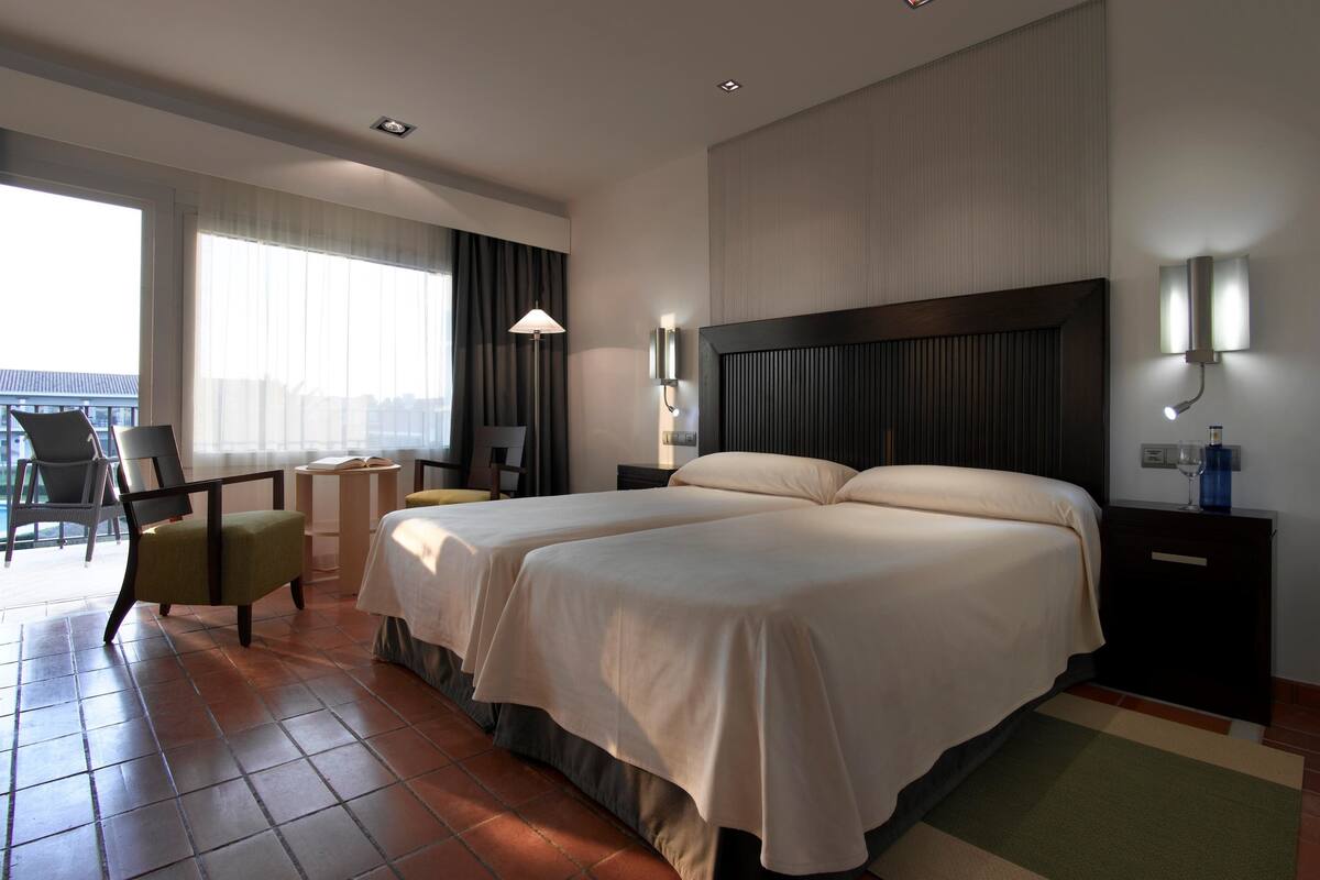 Habitación de hotel con una cama grande, un escritorio con silla y vista a la ciudad por la ventana.