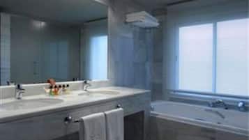 A modern bathroom with two sinks, a large mirror, and a bathtub.