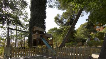 A playground with a wooden slide and swing set, surrounded by trees and a fence.
