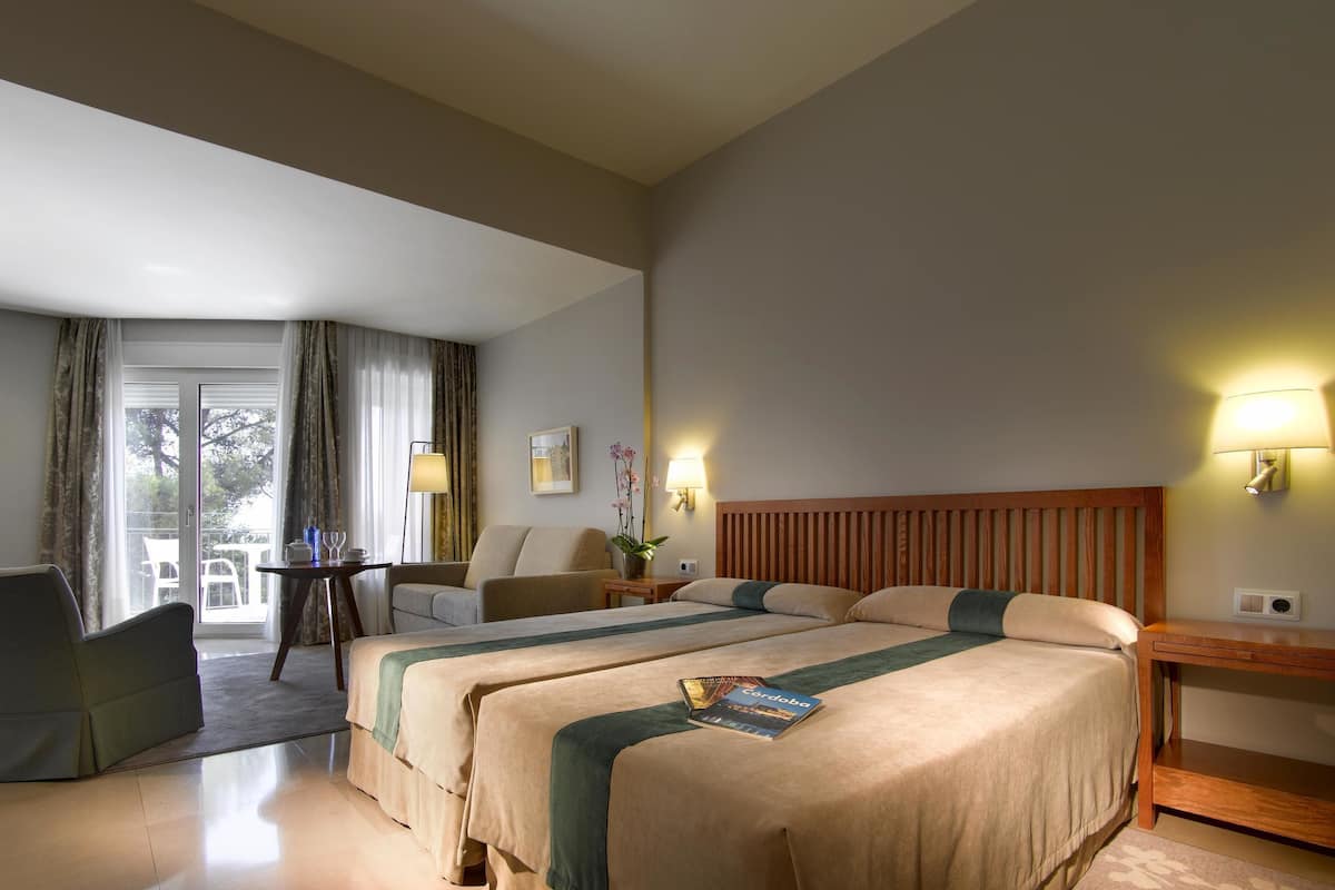 A hotel room with two beds, a sofa, a table, and a lamp.