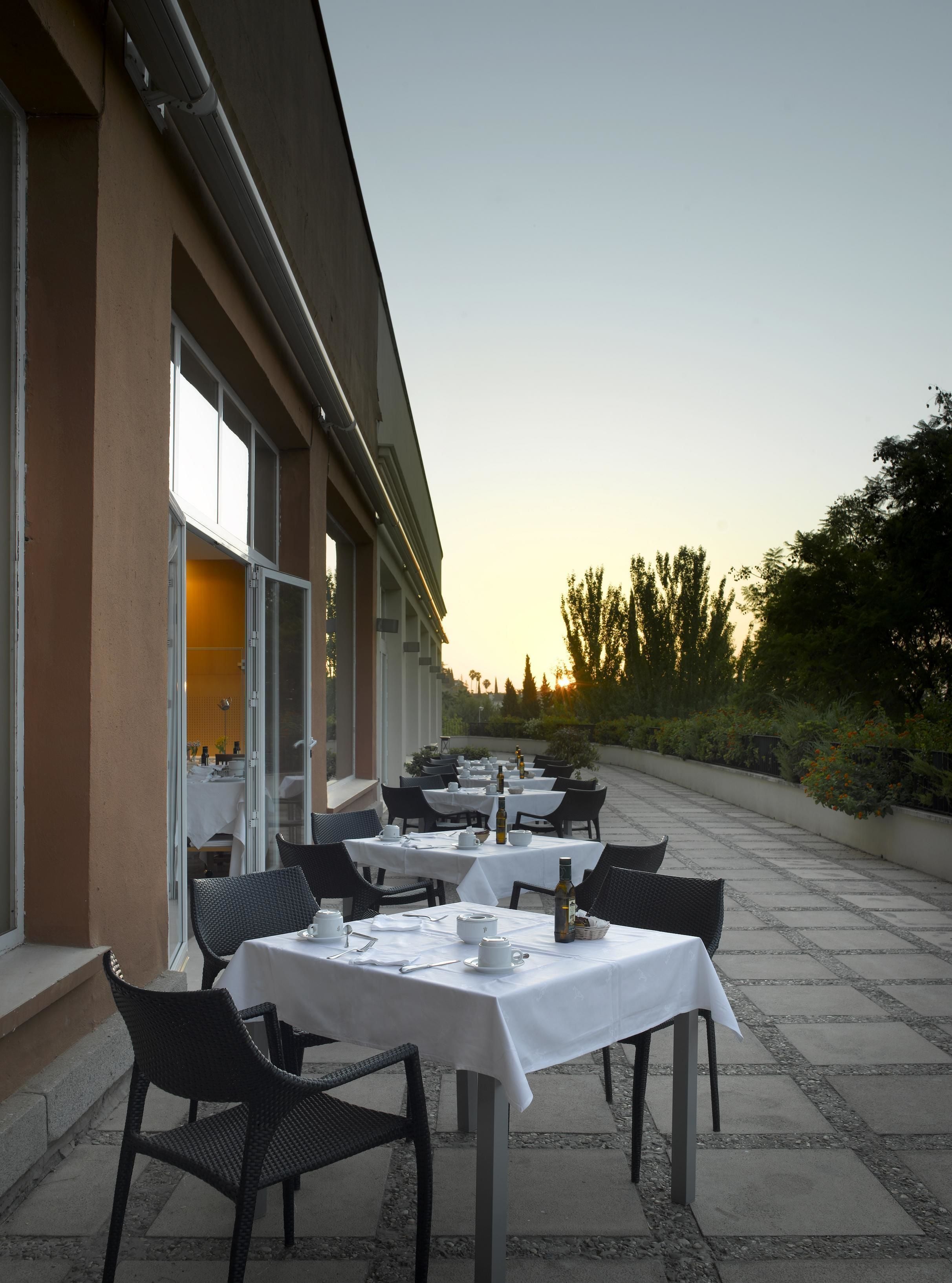 Un espacio de comedor al aire libre con mesas dispuestas para dos, sillas y vistas al atardecer.