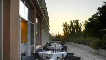 Un espacio de comedor al aire libre con mesas dispuestas para dos, sillas y vistas al atardecer.
