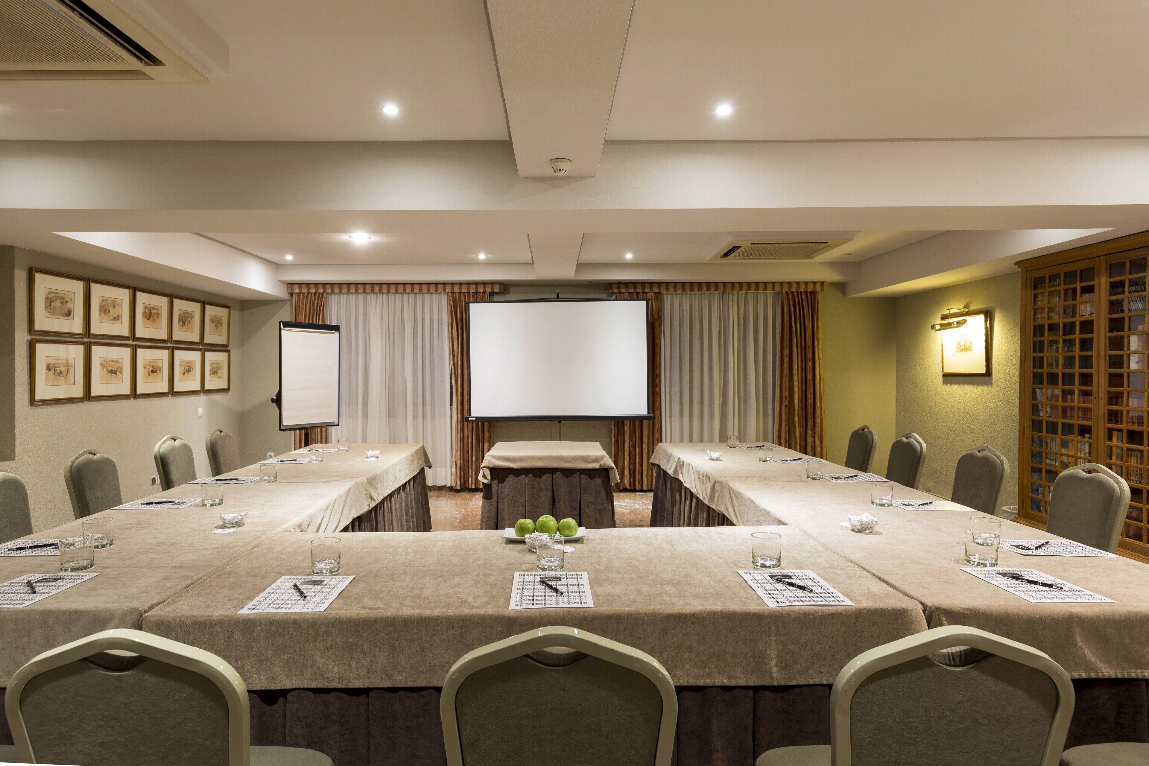 Un salón de conferencias con una mesa larga, sillas, una pantalla de proyector y una pizarra.