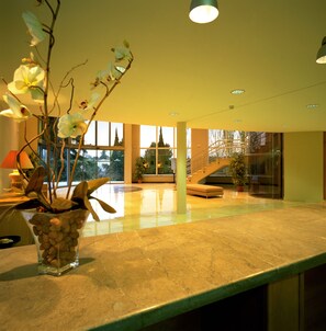 A spacious lobby with a marble floor, a large window offering a view of the outdoors, and a potted plant on the counter. - Parador De Cordoba  (Córdoba)