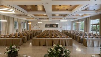 Un salón de conferencias con mesas dispuestas en filas, manteles color beige y centros de mesa con flores.