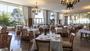Un comedor amplio con varias mesas y sillas, ventanas grandes con cortinas y candelabros.