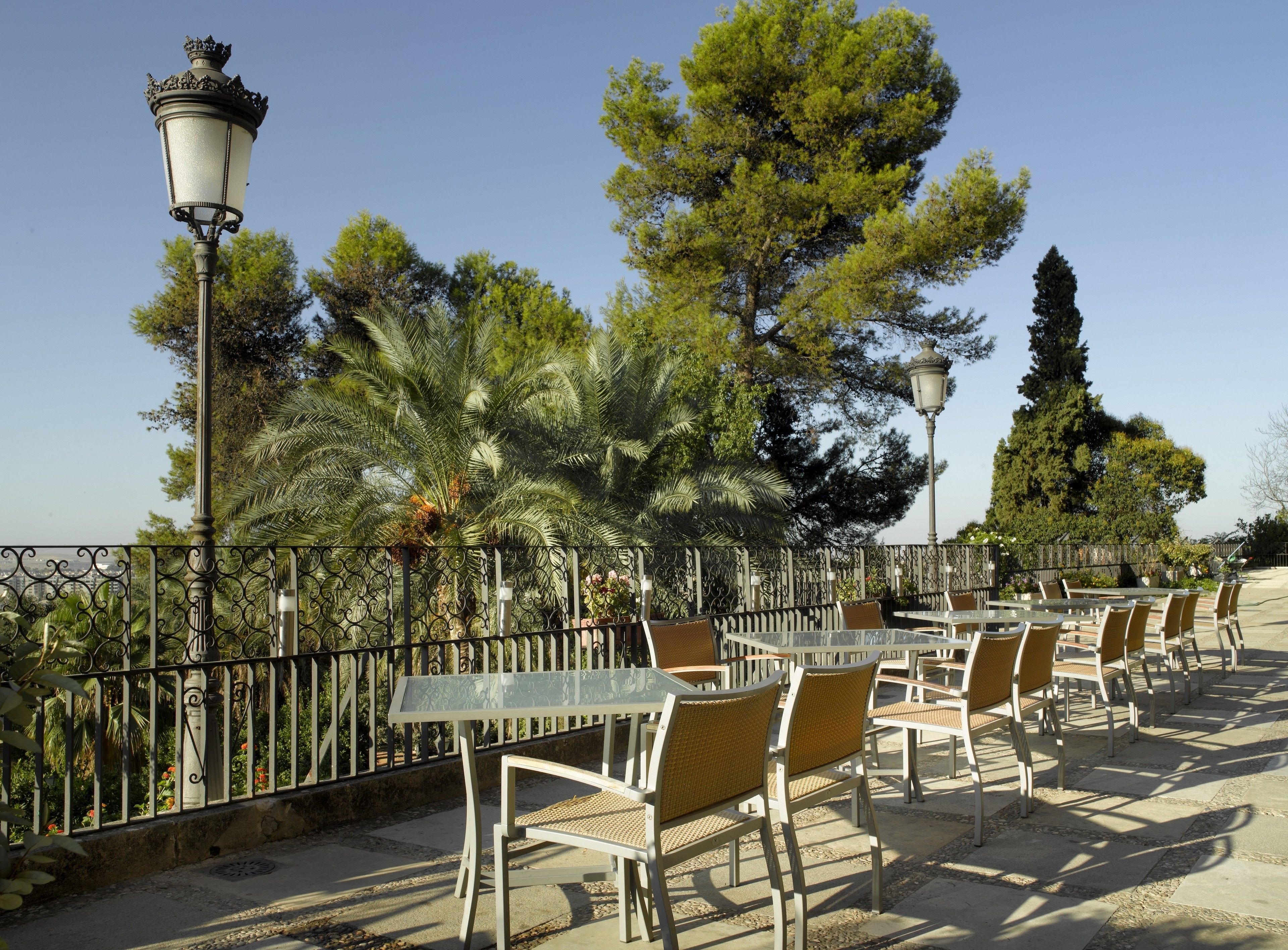Outdoor seating with tables and chairs, surrounded by a decorative fence and trees.