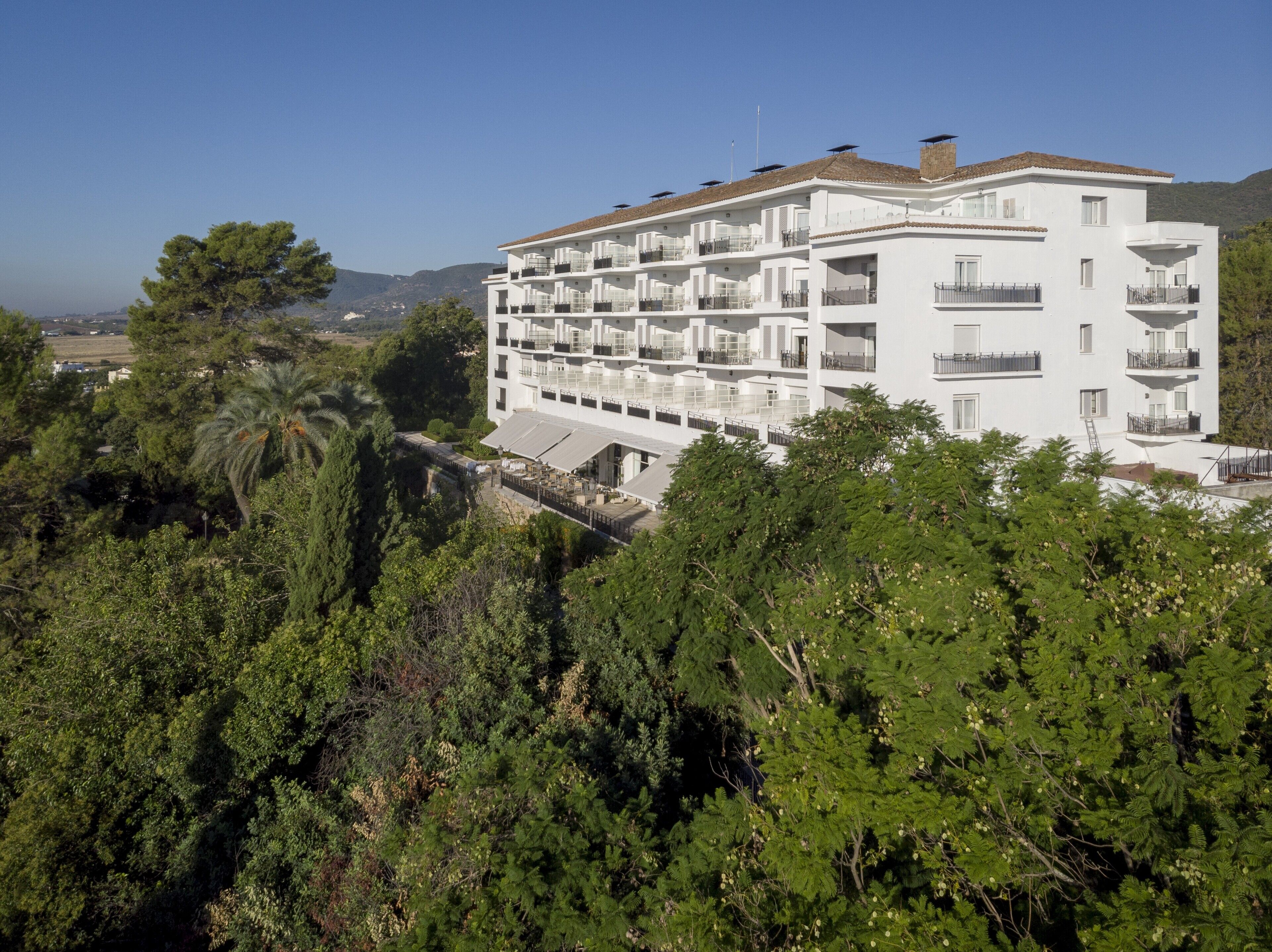 Un hotel de varios pisos con balcones y vistas a la vegetación y colinas circundantes.