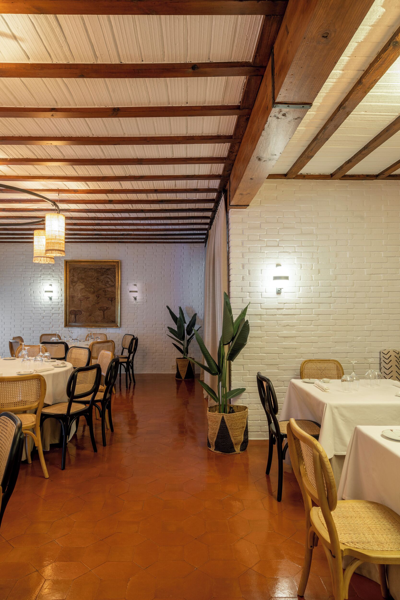 Comedor con vigas de madera, paredes de ladrillo blanco y mesas dispuestas para comer.