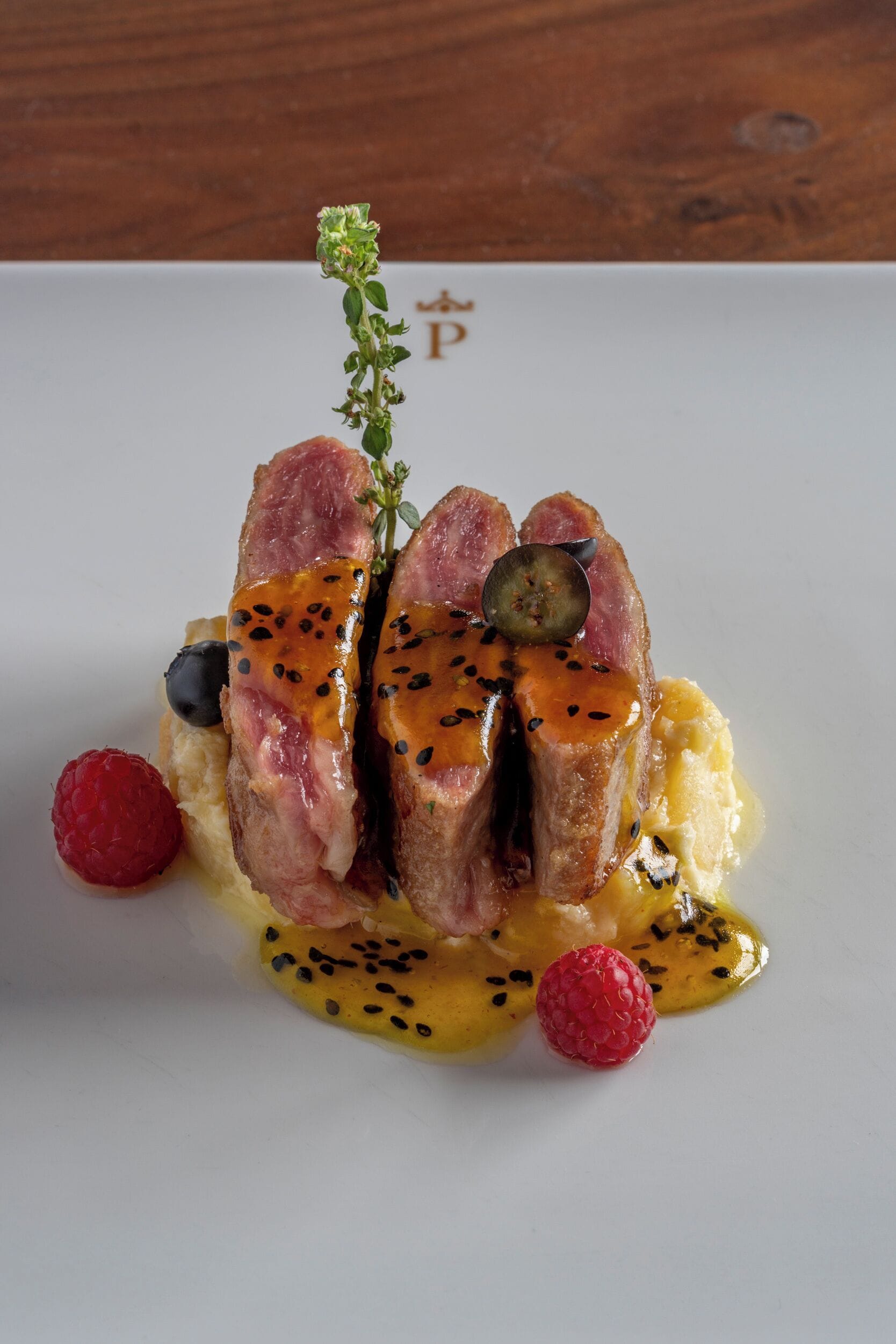 Un plat composé de viande, de baies et d’une branche d’herbes aromatiques, le tout présenté sur une assiette blanche.