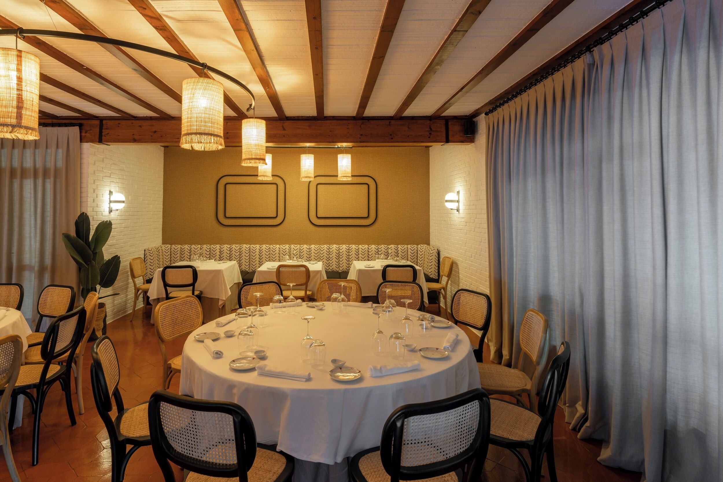 A dining area with round tables, wicker chairs, and hanging light fixtures.