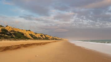 Uma praia com areal arenoso e um rochedo ao fundo.