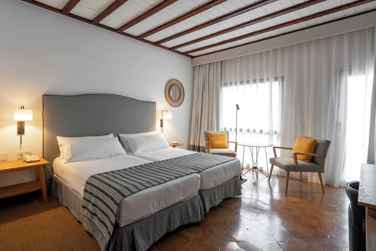 Habitación de hotel con una cama grande, dos mesitas de noche, un escritorio, una silla y una ventana con cortinas.