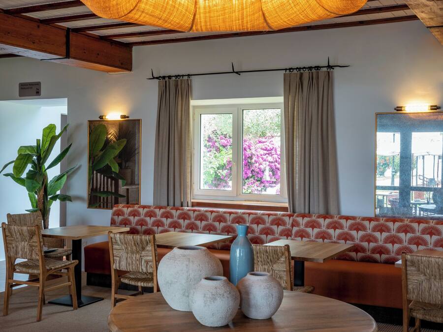 A cozy room with a round wooden table, wicker chairs, a red and white patterned sofa, and a large woven light fixture.