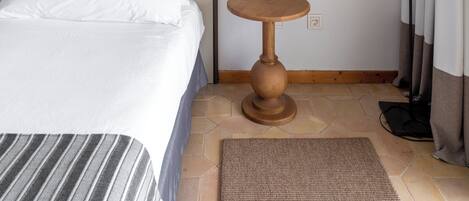 A hotel room with a large bed, a round mirror, a bedside table, a lamp, and a view of the outdoors.