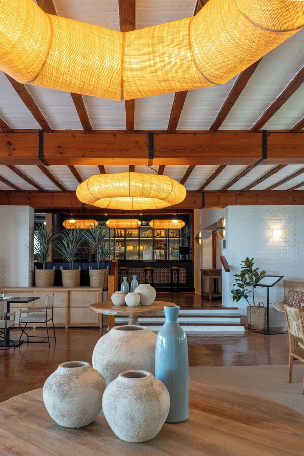 Un intérieur spacieux avec de hauts plafonds, des poutres en bois et un espace salon central agrémenté d’une table et de chaises.